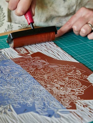 A roller with ink going over a lino plate, ready for printing